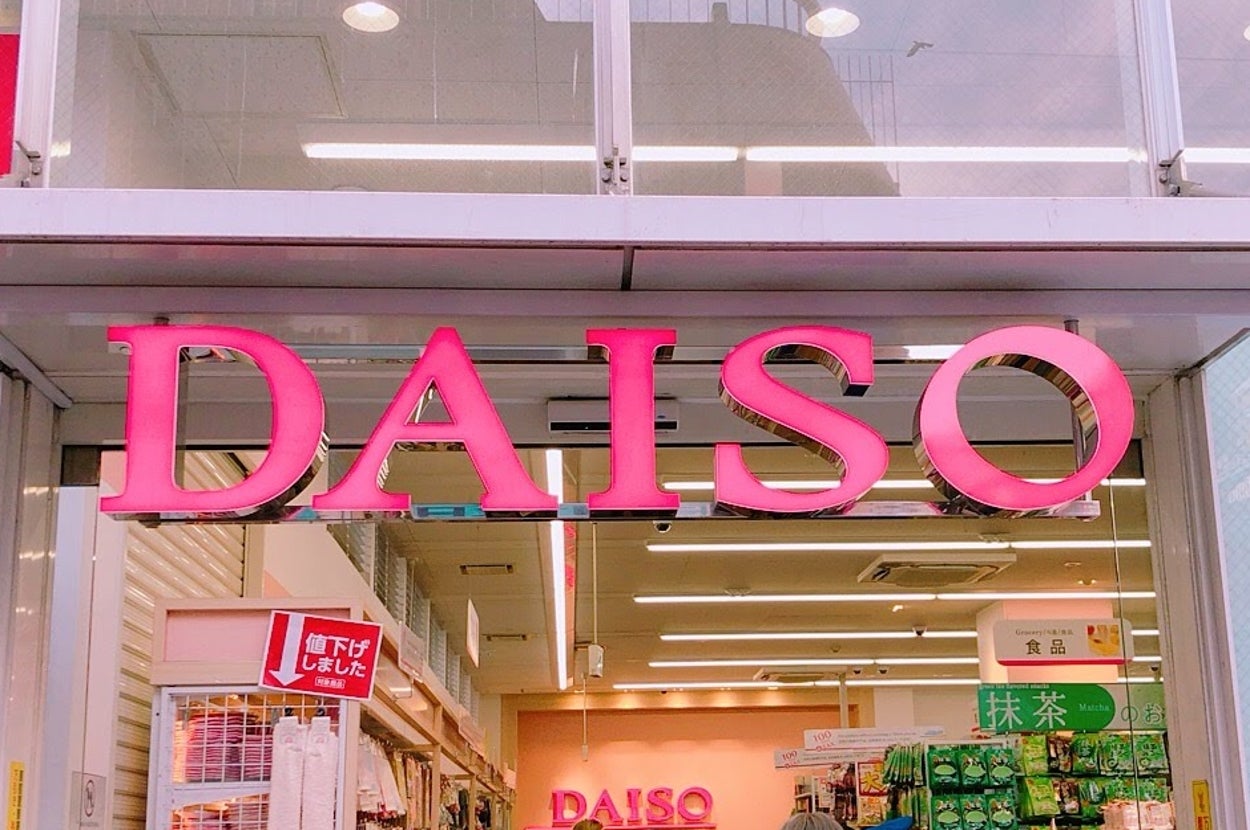 DAISOの店舗入口で、買い物客が出入りしています。商品棚には多様な商品が並んでいます。