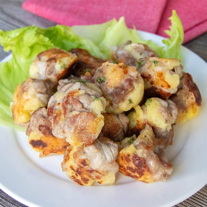 じゃがいもと豚こま切れ肉、チーズで作られたミートボールが盛られた白い皿。皿の縁にレタスの葉が添えられています。