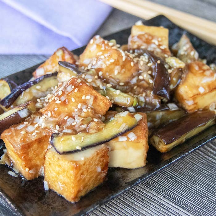 厚揚げとなすのねぎだれ炒めの料理が黒い皿にのり、白いりごまがかかっています。