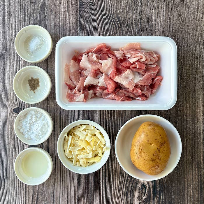食材の上からの写真。豚こま切れ肉、じゃがいも、ピザ用チーズ、塩、調味料が小皿に分かれている。