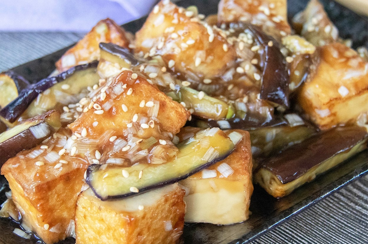 厚揚げとなすのねぎだれ炒めの料理が黒い皿にのり、白いりごまがかかっています。