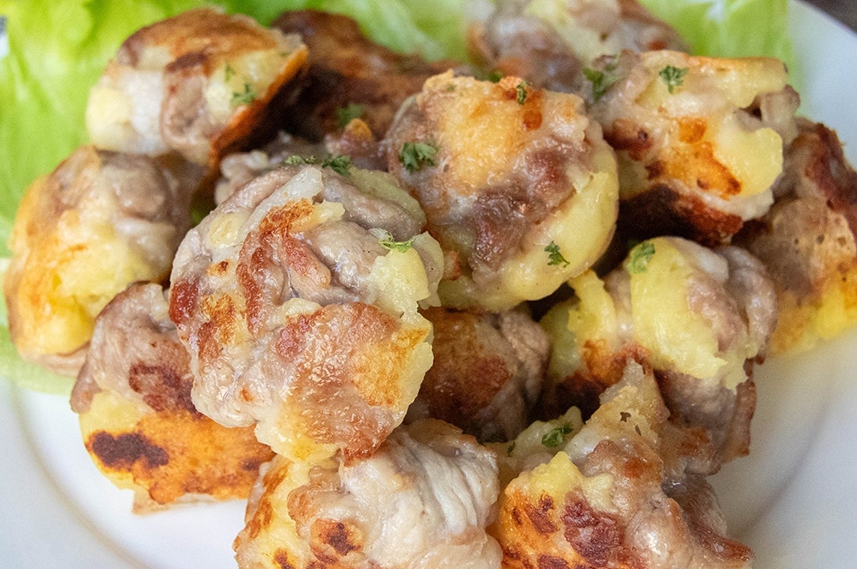 じゃがいもと豚こま切れ肉、チーズで作られたミートボールが盛られた白い皿。皿の縁にレタスの葉が添えられています。