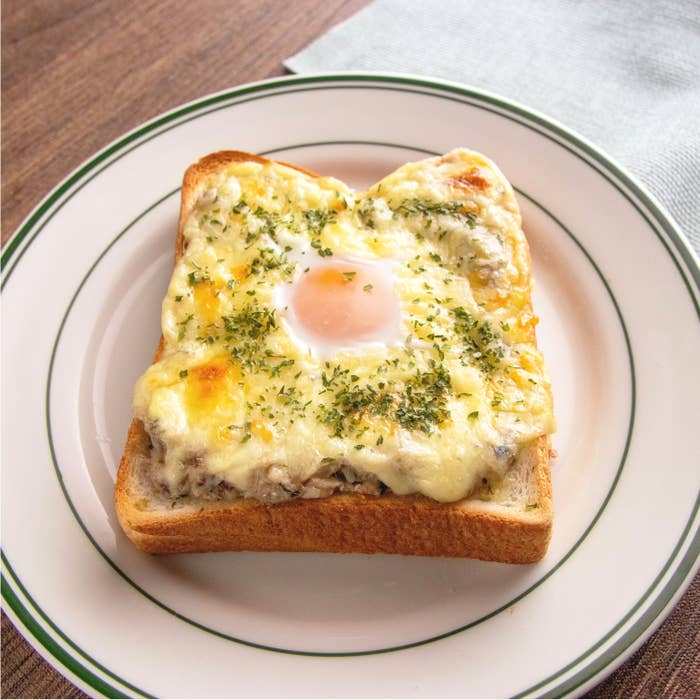 食パンの上にチーズ、卵、パセリがトッピングされたトーストが白いお皿にのっている。