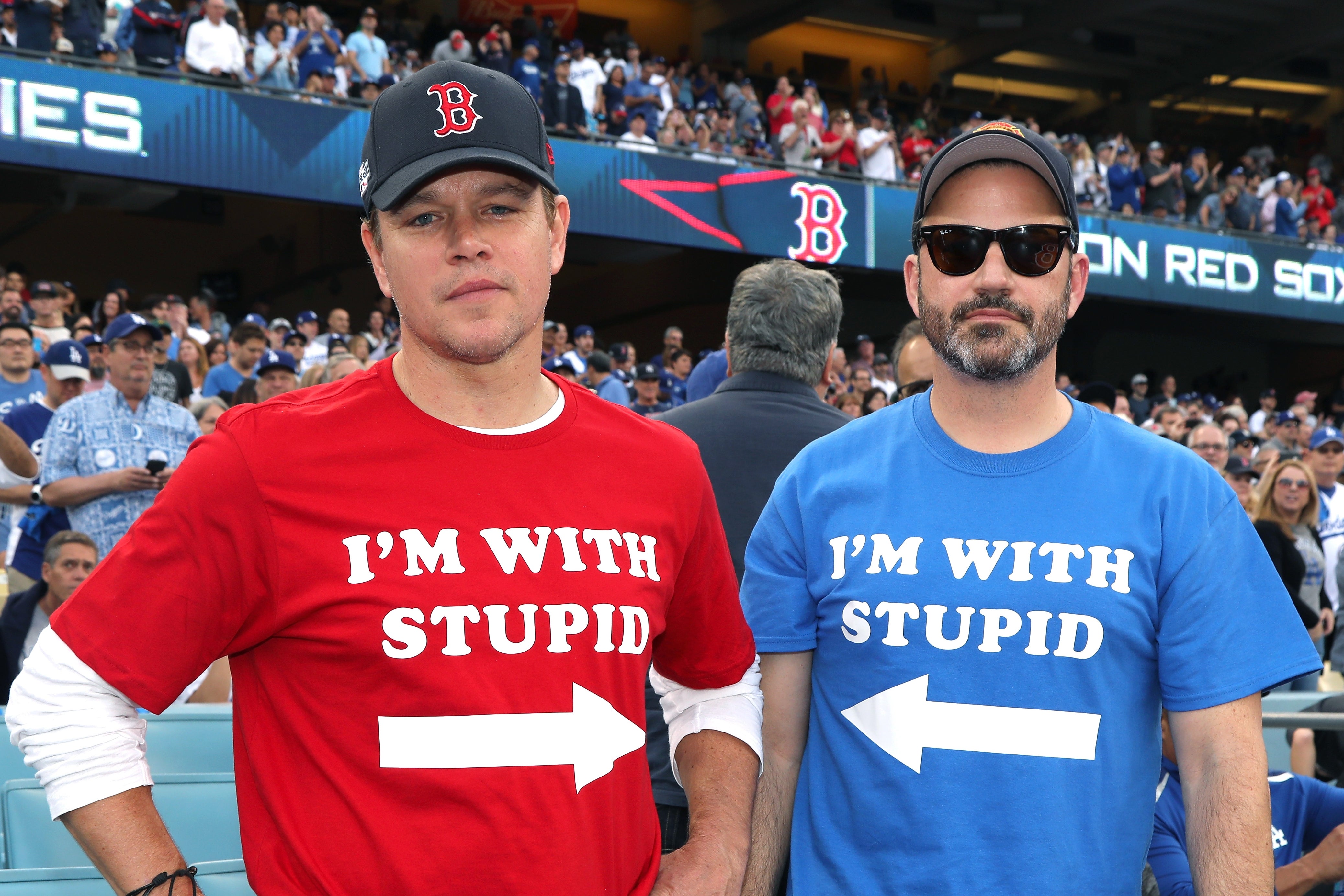 Two men wearing "I'm with stupid" T-shirts and baseball caps stand in a stadium, indicating a playful moment at a sports event