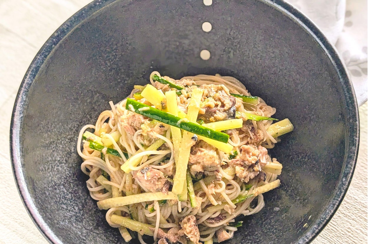 黒いボウルに入った冷製そば麺のサラダ。割いたキュウリとツナ、ゴマが添えられている。