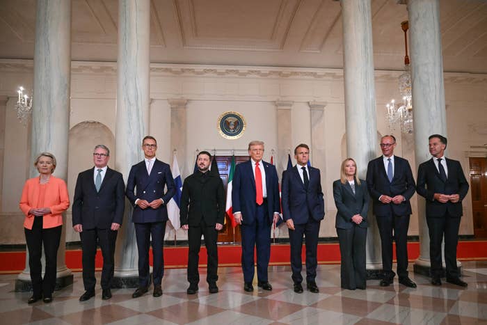 A radical of 9 individuals, including men and women, stands formally successful a expansive country with pillars and a statesmanlike seal supra them