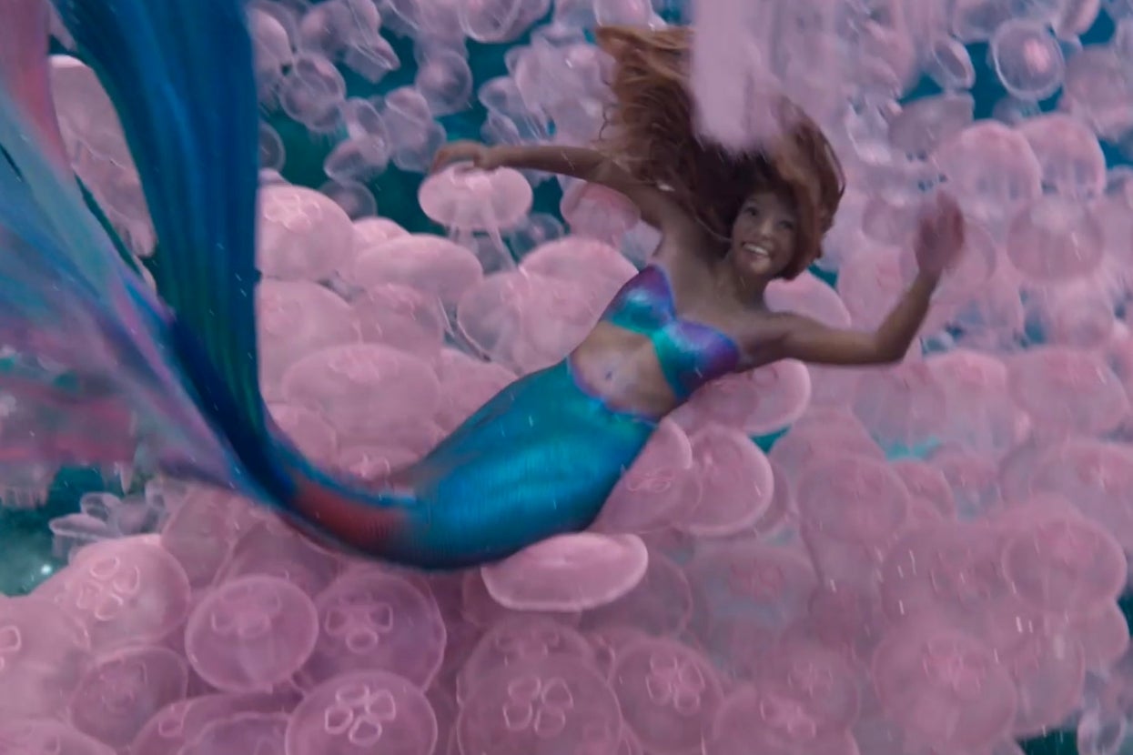 Person swimming underwater in a mermaid costume with pink jellyfish surrounding them