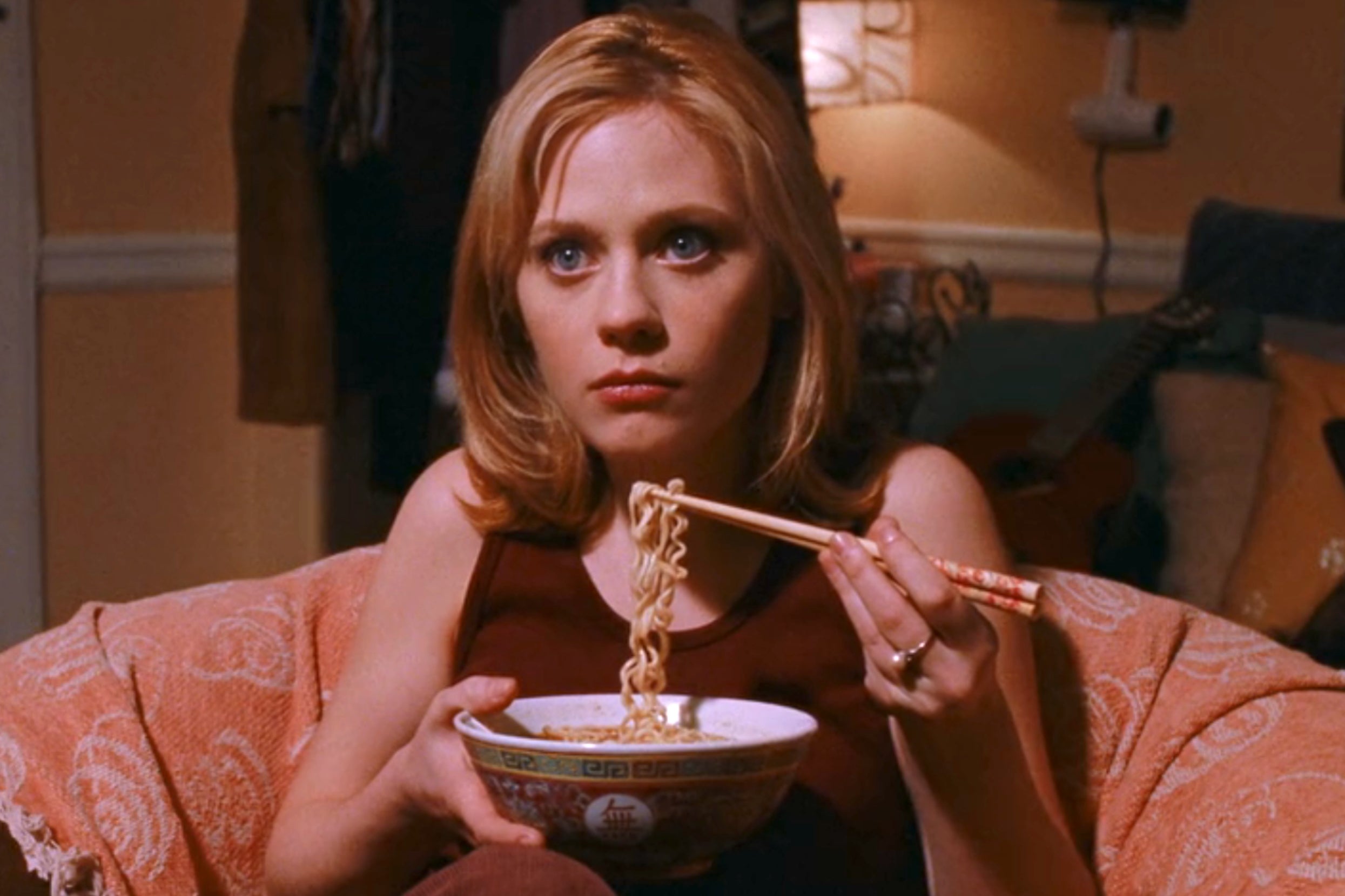 Zooey Deschanel sitting on a couch, eating ramen with chopsticks, as Jovie in Elf