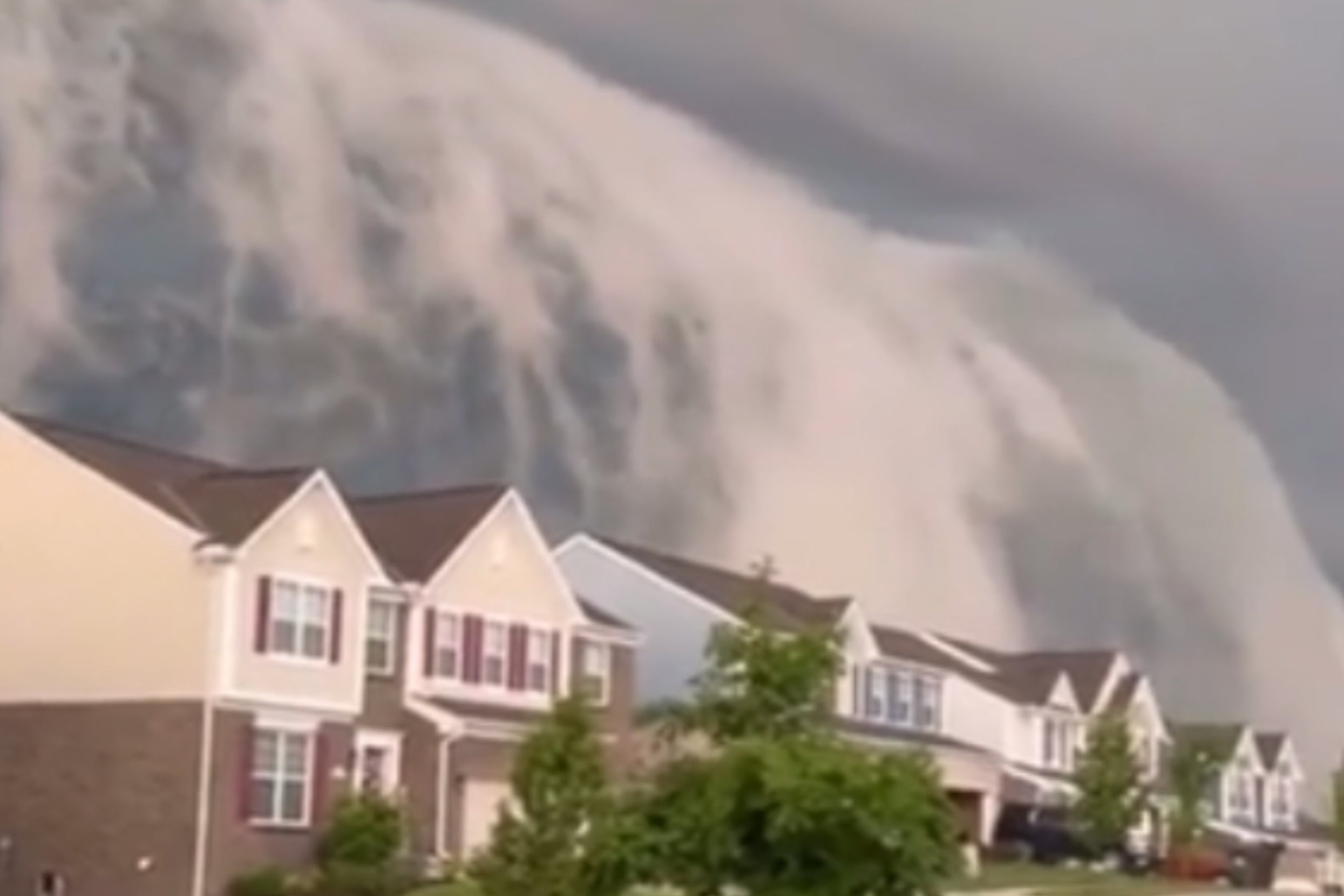 Giant wave illusion in the sky towers over suburban street with houses and trees, creating a surreal and dramatic scene