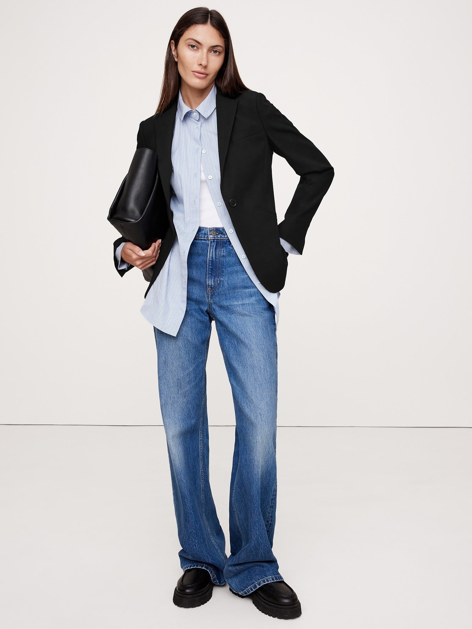 Person wearing a tailored blazer, untucked shirt, wide-leg jeans, and holding a clutch bag, styled for a casual yet chic buying  experience
