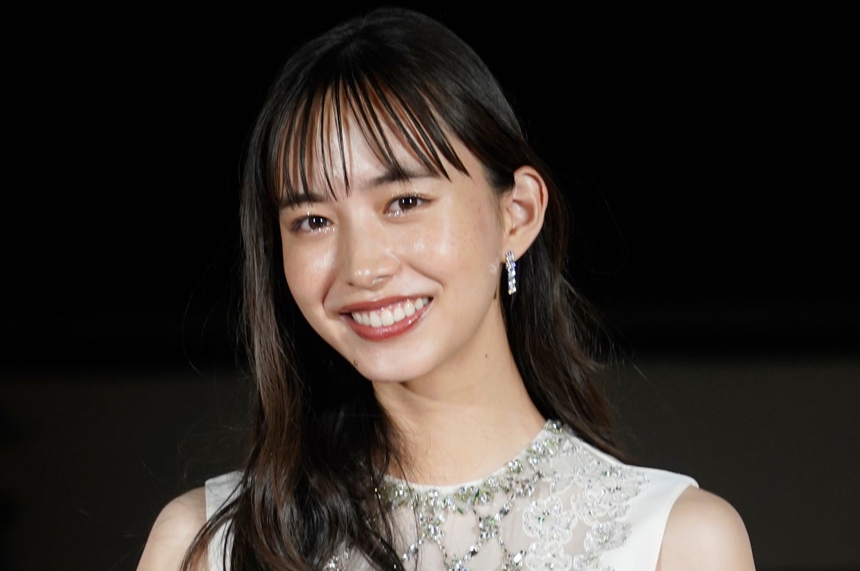 有名人が短い袖の白いビーズ付きドレスを着て笑っている。