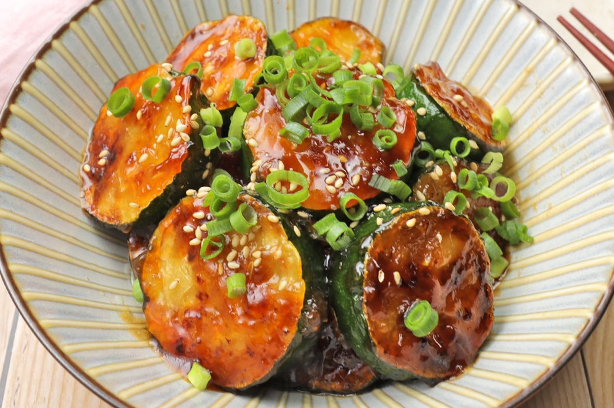 薄切りのズッキーニが照り焼きソースで味付けされ、タマネギとゴマがトッピングされた料理の写真。