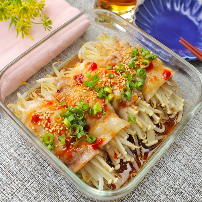 ガラスの容器に入った料理。もやしときのこ、肉がのっており、ねぎとゴマが散らされている。