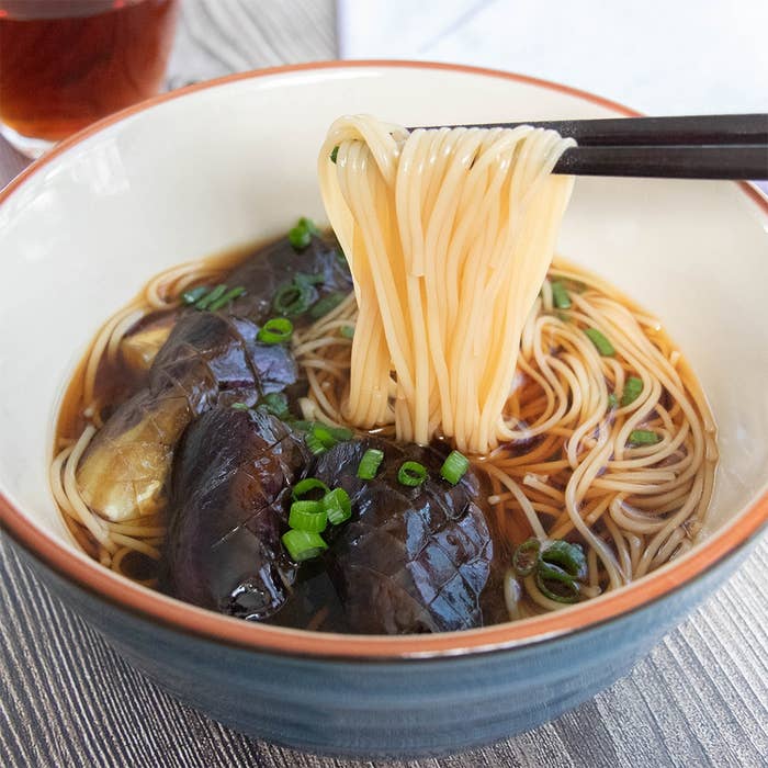 箸で持ち上げられたそうめん。丼には焼き浸しにしたなすが1本分入っている。
