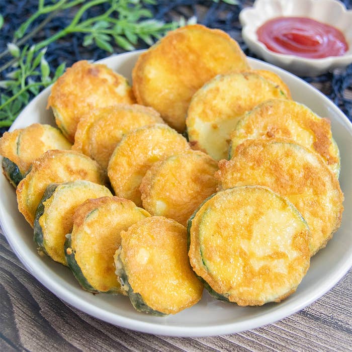皿に並べられたズッキーニのピカタ。粉チーズと卵の衣を付けて焼いてある。トマトケチャップが添えられている。