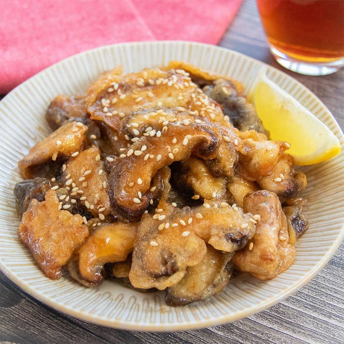 皿に盛られた揚げ焼きにしたしいたけの料理。レモンと白いりごまが添えられています。