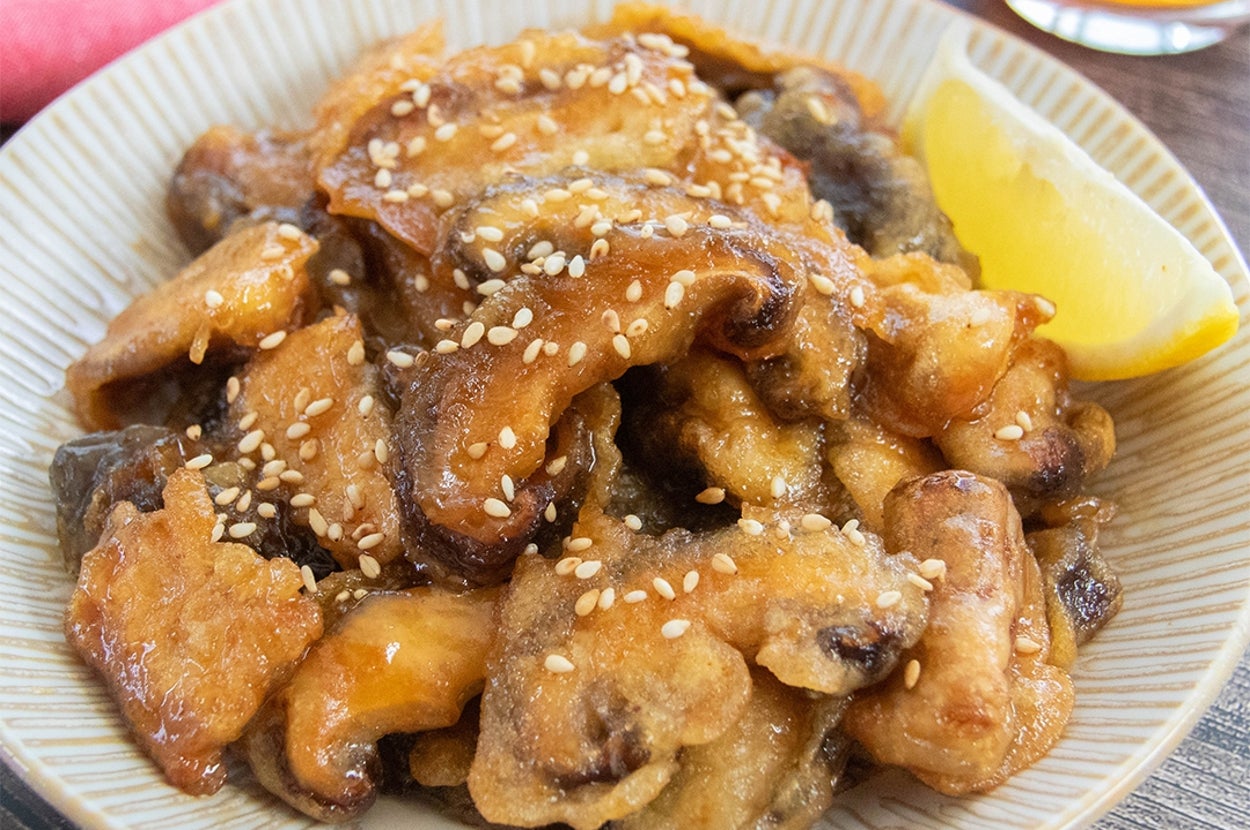 皿に盛られた揚げ焼きにしたしいたけの料理。レモンと白いりごまが添えられています。