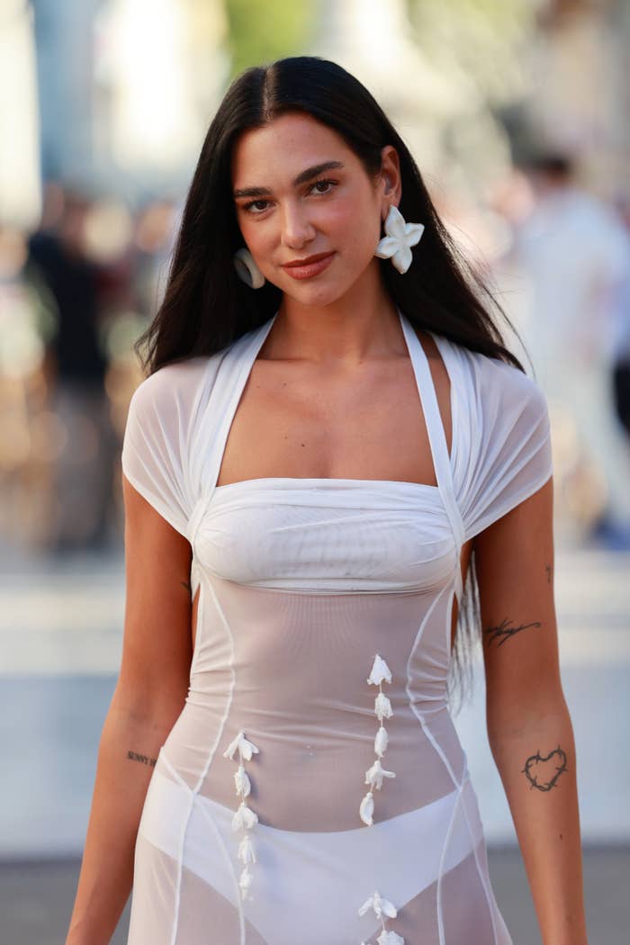 A pistillate successful a stylish, semi-sheer achromatic formal with floral decorations poses confidently outdoors. She wears ample angiosperm earrings