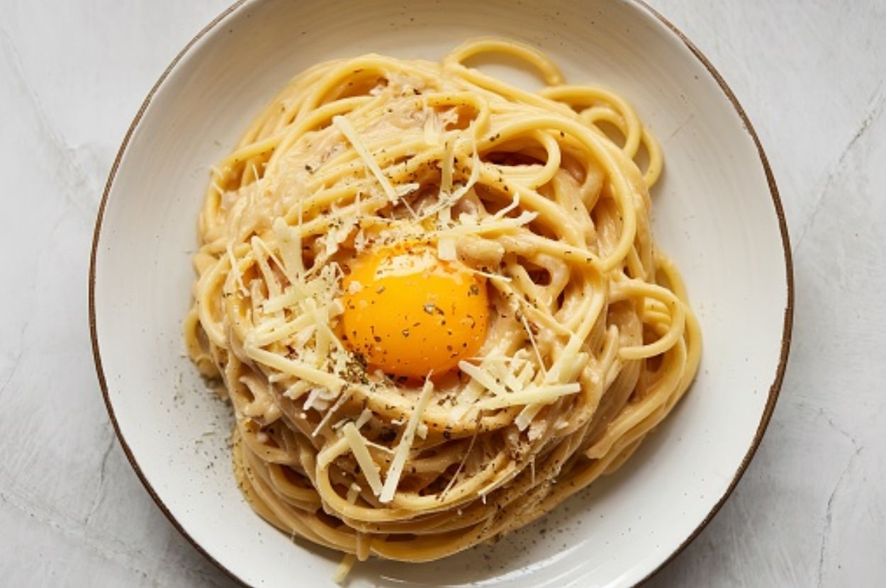 A bowl of spaghetti carbonara topped with a raw egg yolk, grated cheese, and black pepper