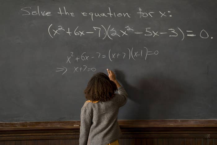 Person solving a quadratic equation written connected a chalkboard successful a schoolroom setting