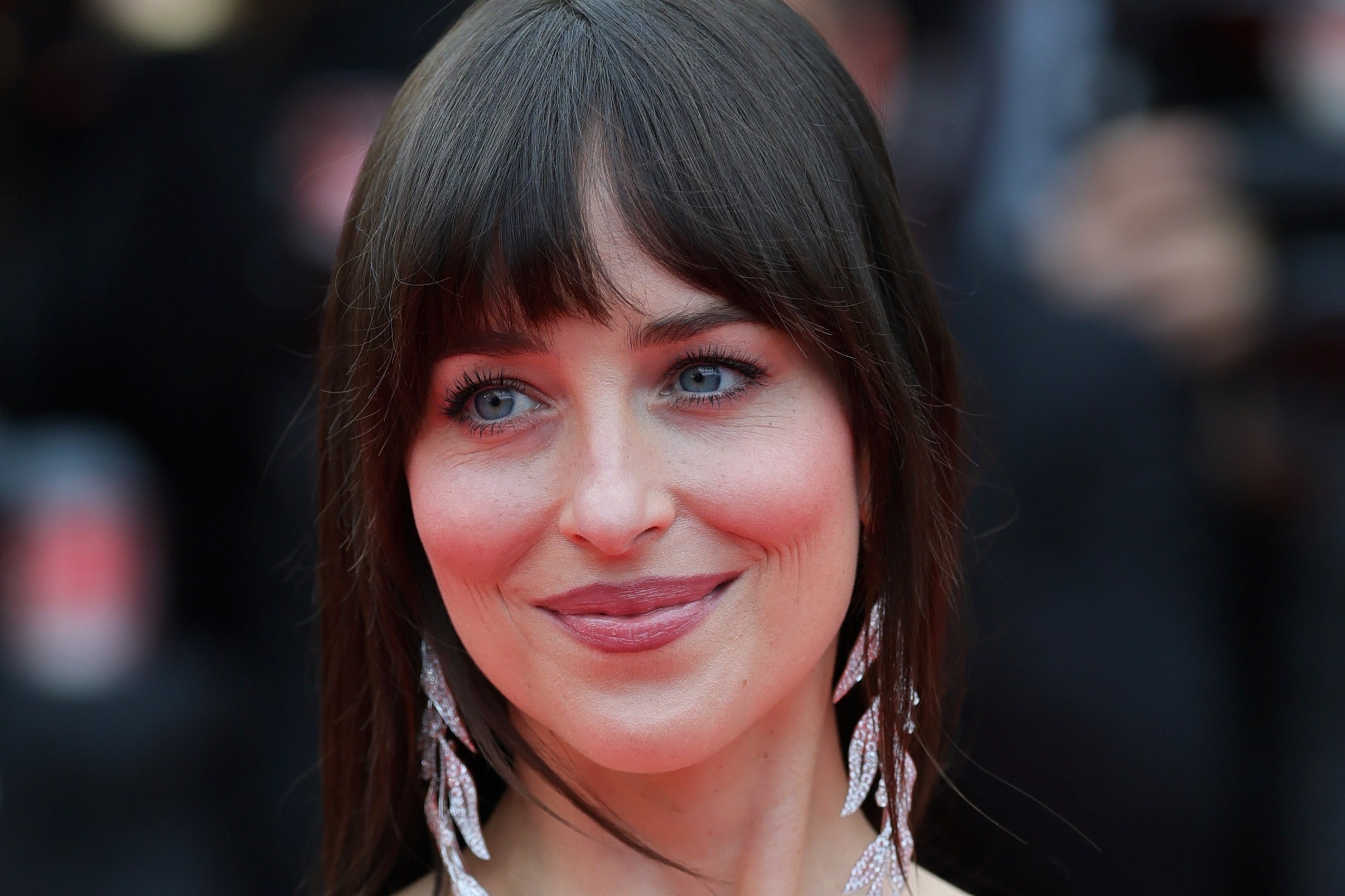 Dakota Johnson on a red carpet in a strapless textured dress, with long drop earrings, smiling slightly