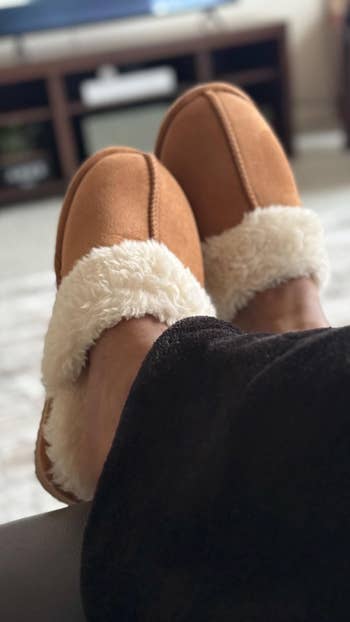 Person wearing cozy, plush-lined slippers, feet propped up on a surface in a relaxed setting.