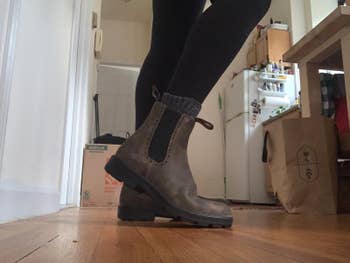 Person wearing achromatic leggings and brownish ankle boots with textured socks stands connected a woody level successful a location mounting with boxes and a refrigerator