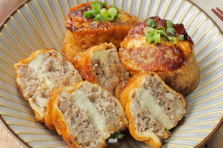 お皿に盛られた詰め物入りの油揚げ料理。カットされ中の具材が見える。葱がトッピングされている。
