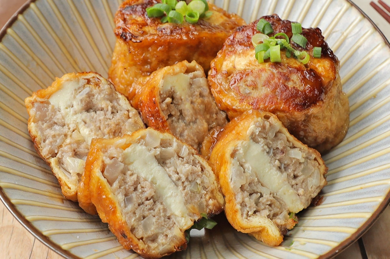 お皿に盛られた詰め物入りの油揚げ料理。カットされ中の具材が見える。葱がトッピングされている。