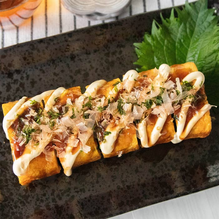 お好み焼き風卵焼きが黒い皿に並んでいる。ソース、マヨネーズ、かつお節、青のりがかかっている。