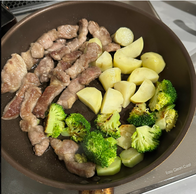 フライパンで調理中の肉、じゃがいも、ブロッコリー。