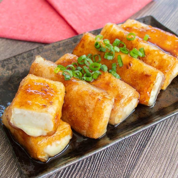 長方形にカットされた厚揚げ豆腐とスライスチーズをライスペーパーで巻いて焼いたおつまみ。甘辛い焼肉のたれで絡められ、上に小ネギがのっている。