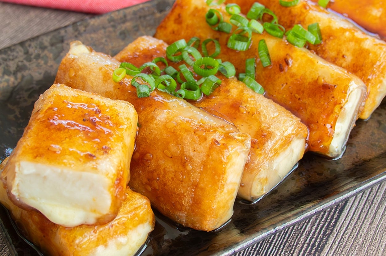 長方形にカットされた厚揚げ豆腐とスライスチーズをライスペーパーで巻いて焼いたおつまみ。甘辛い焼肉のたれで絡められ、上に小ネギがのっている。