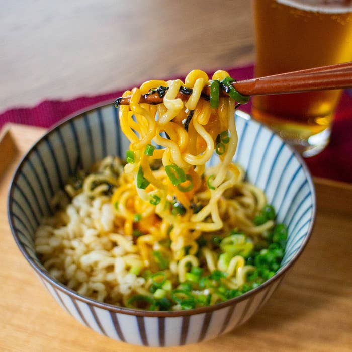 箸で持ち上げられたネギ入りラーメンのボウル。隣にビールグラスがある。