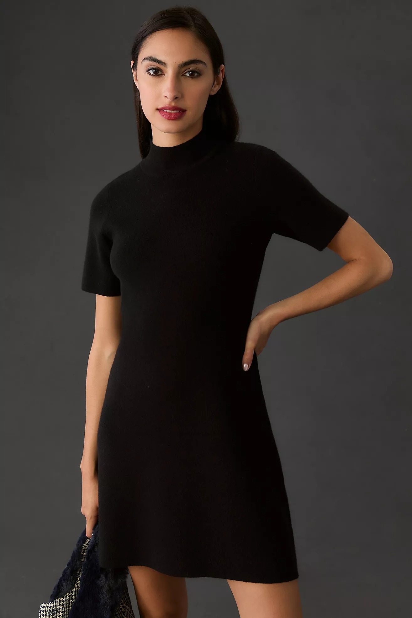 Person wearing a stylish short-sleeve, knee-length black dress, posing confidently with hand on hip, suitable for casual or formal occasions