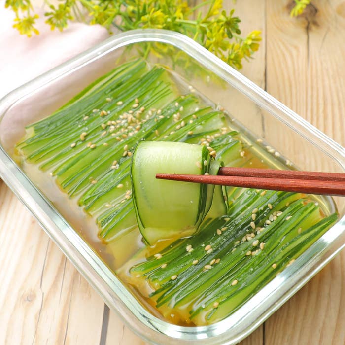 ガラス容器に並べられたきゅうりと細長い野菜の浅漬け。箸でひとつ持ち上げた様子。