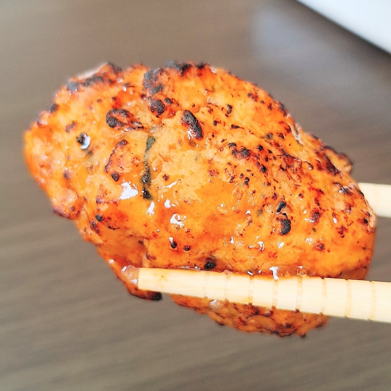 箸で持たれた焼き鶏肉のクローズアップ。ジュージーで美味しそう。