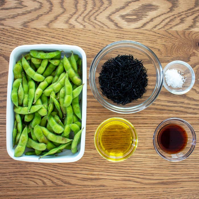 木のテーブルに置かれた枝豆の入ったトレイ、ひじき、塩、オリーブオイル、醤油がそれぞれ器に入っている。