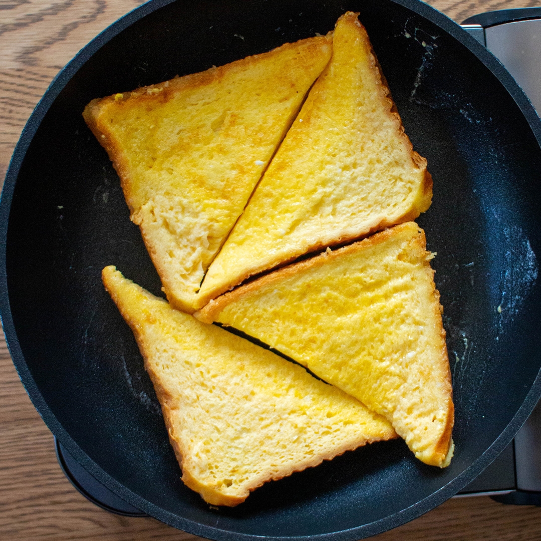 フライパンで焼いている3枚の三角形のフレンチトースト。