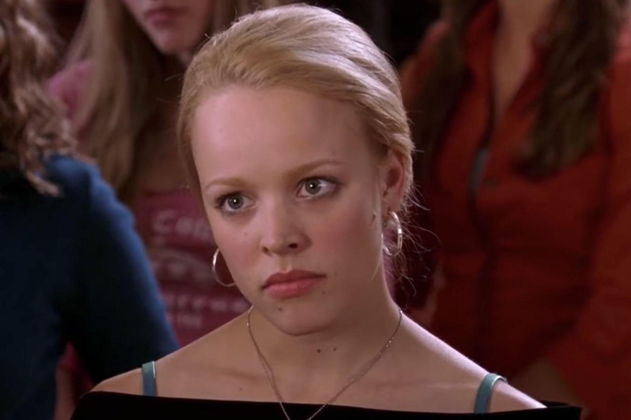 Rachel McAdams as Regina George in "Mean Girls" with hoop earrings and a serious expression stands amidst a crowd, wearing an off-shoulder top
