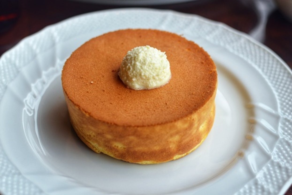 A fluffy, round sponge cake with a dollop of cream on top, served on a decorative white plate