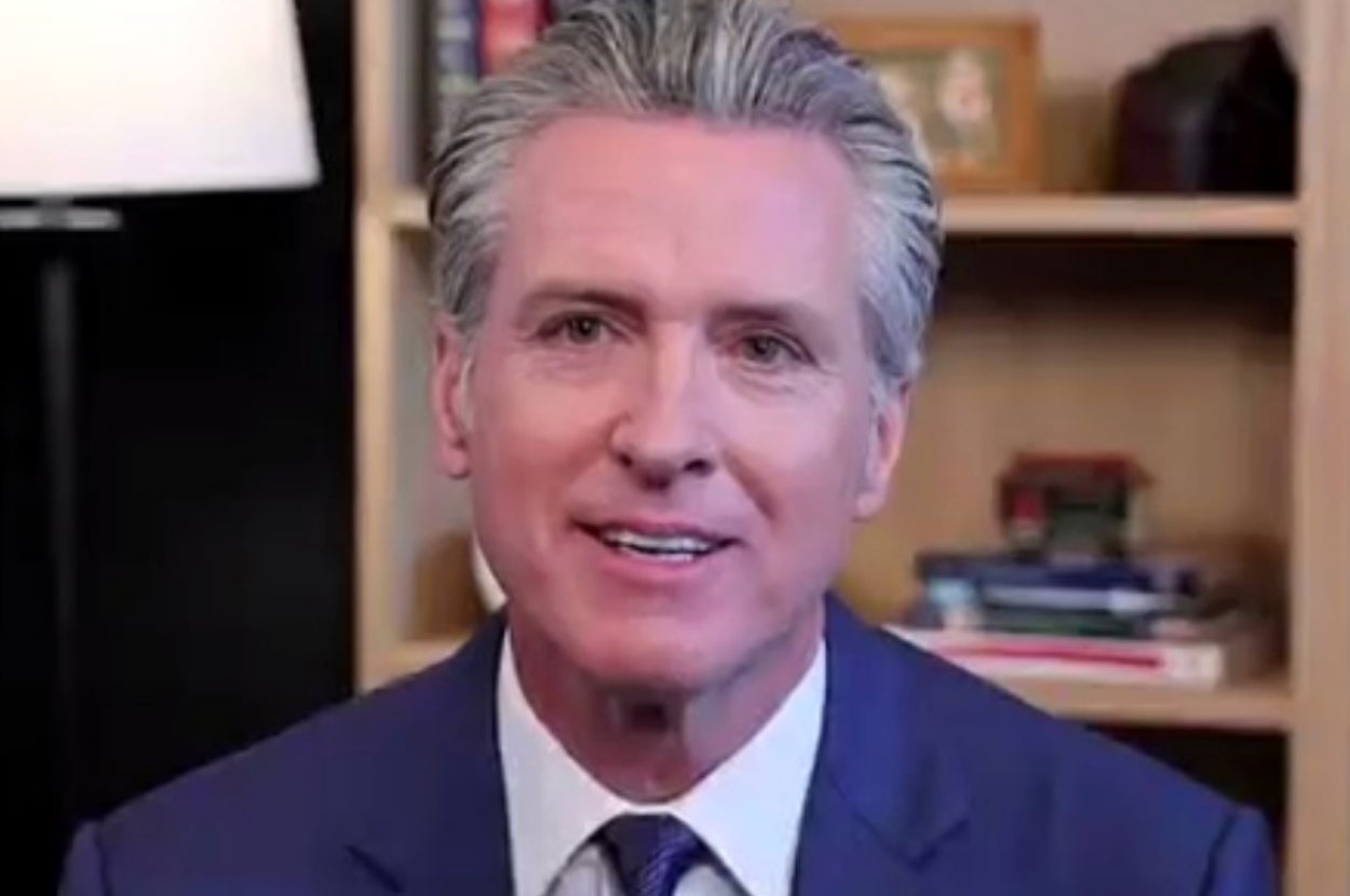 A person in a suit speaks in a room with bookshelves in the background, possibly addressing an audience