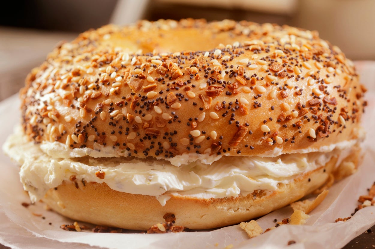 Bagel topped with sesame and poppy seeds, filled with cream cheese, on a paper wrapper