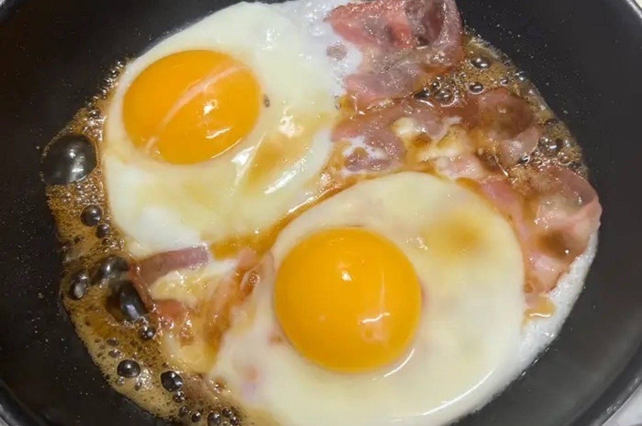 フライパンでベーコンと目玉焼きを調理している様子。