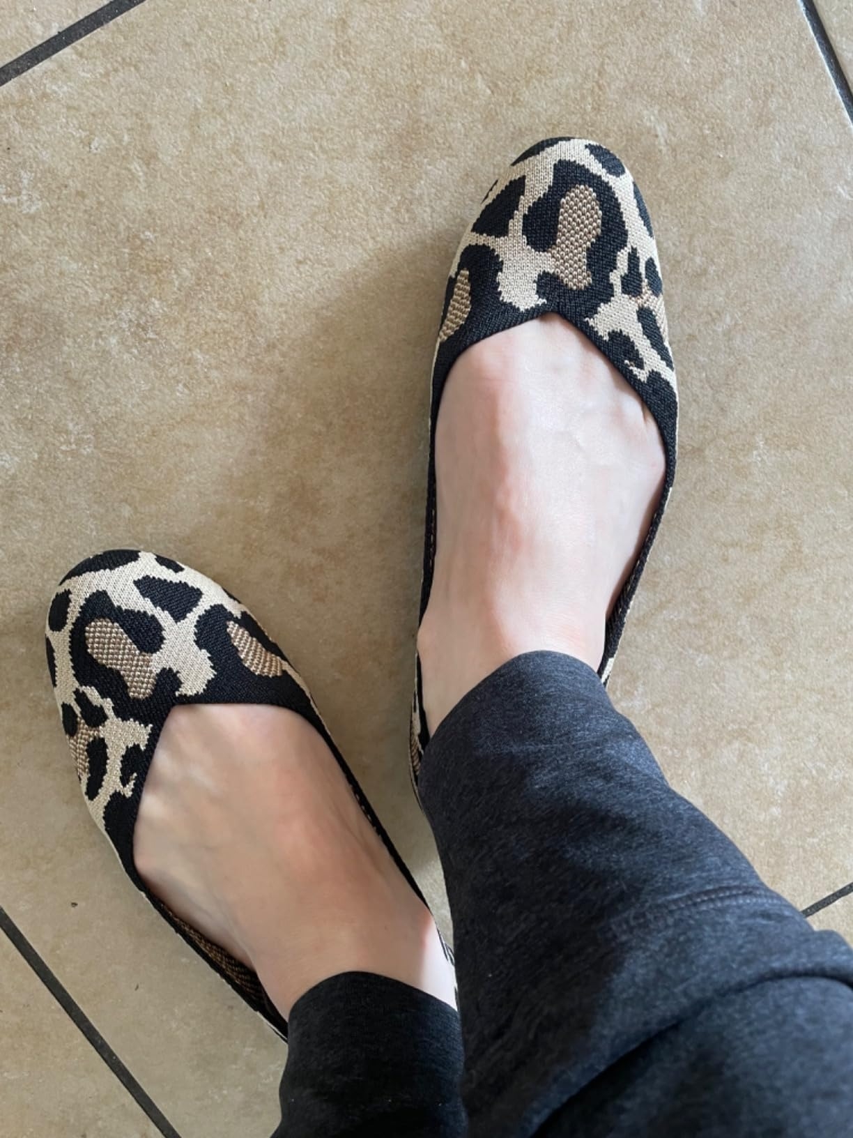Person wearing leopard-print ballet flats, standing on a tiled floor