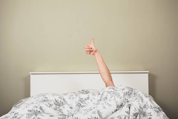 A person&#x27;s arm extends from under a blanket, giving a thumbs up, while lying in bed