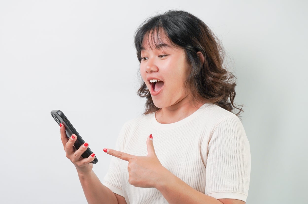 Person smiling and pointing at a smartphone, appearing surprised or excited while looking at the screen