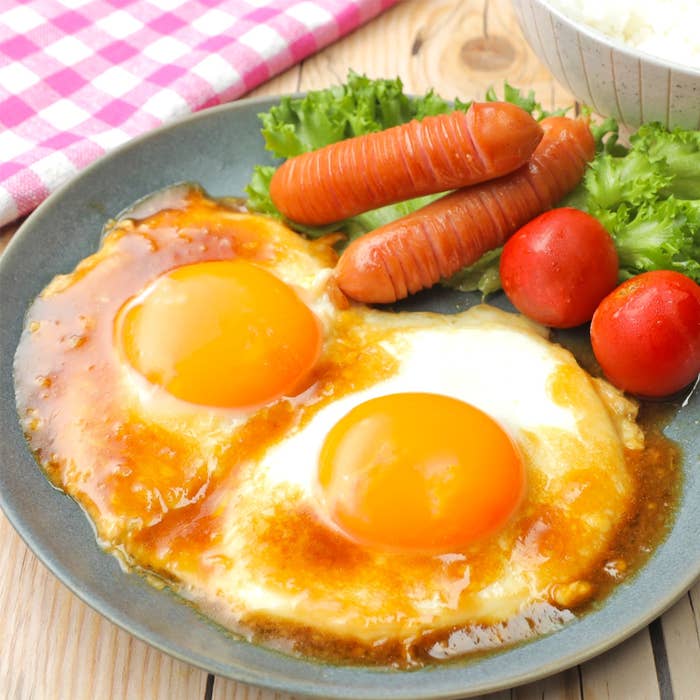 目玉焼き2枚、ソーセージ、トマト、レタスがプレートに盛り付けられている朝食メニュー。