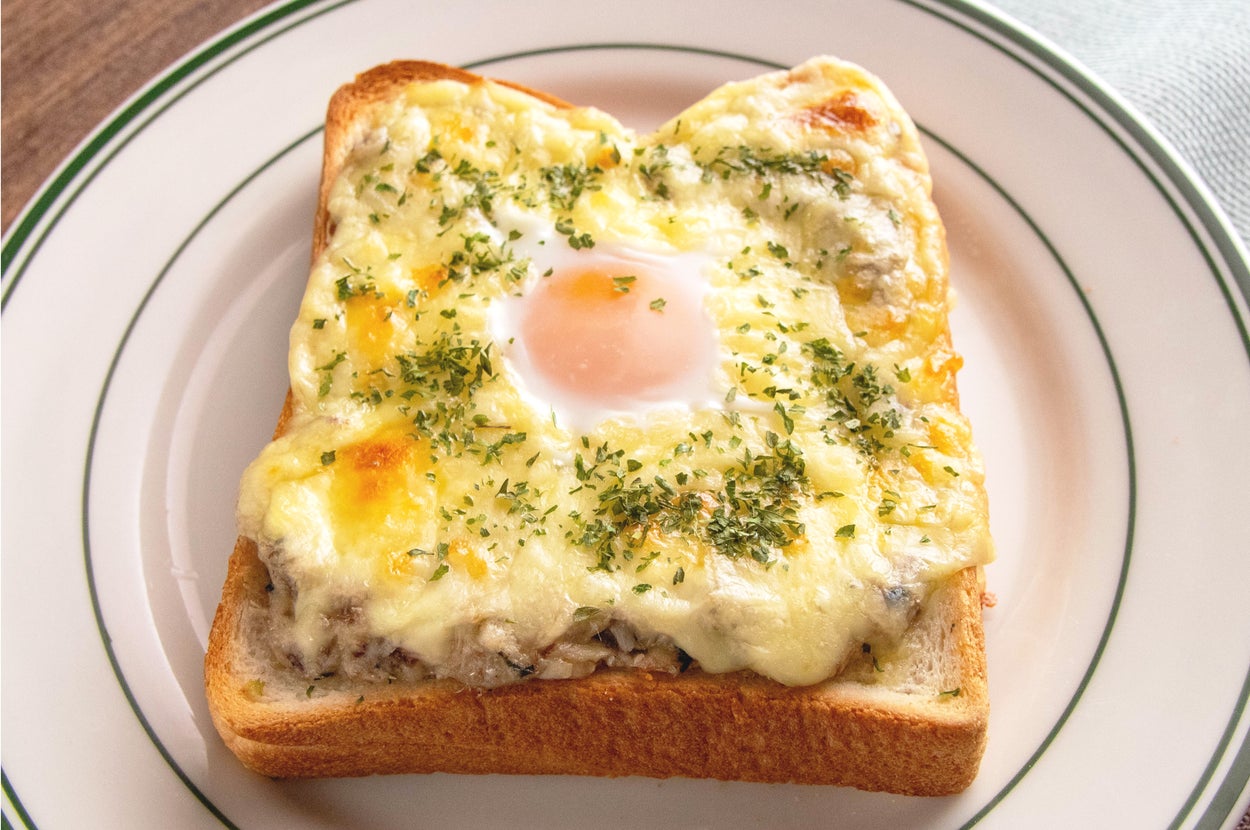 トーストの上にチーズ、目玉焼き、ハーブがのった料理が白い皿に盛られています。