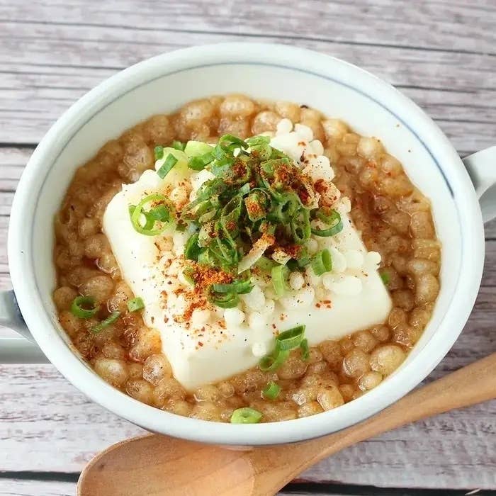 ヘルシーな豆腐丼、一杯の器に豆腐、ネギ、揚げ玉がトッピングされ、和風の木製スプーンが添えられています。